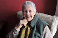 an older woman sitting in a chair with a green scarf